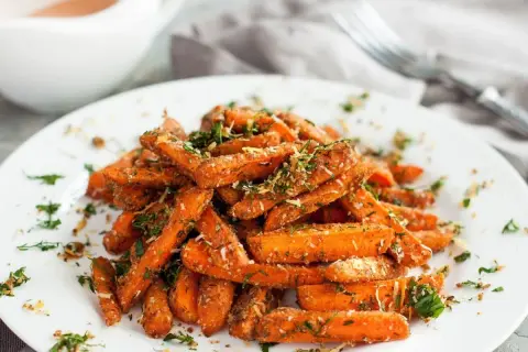 Karmelizowana marchewka, posypana ziołami i parmezanem, podana na białym talerzu.