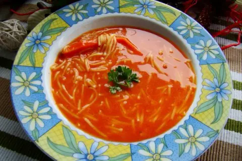 Zupa pomidorowa z przecieru z makaronem nitki i natką pietruszki, podana w kolorowym talerzu.