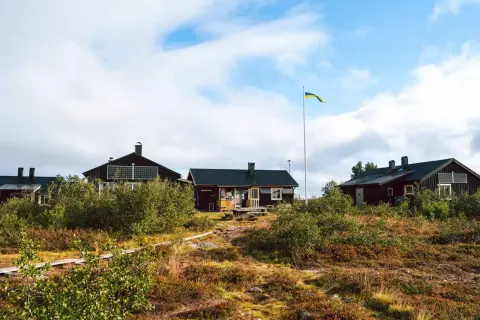 Mörka trähus med solpaneler och en svensk flagga som vajar vid ett vandrarhem i Dalarna.