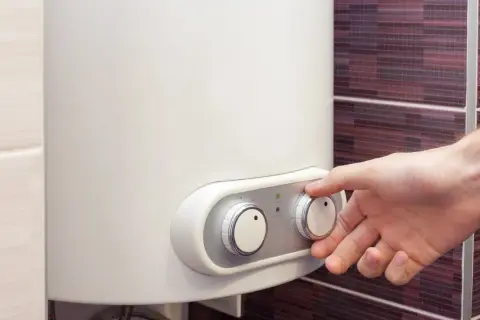 Dłoń reguluje pokrętłem termę elektryczną 50l. Zielona lampka sygnalizuje pracę urządzenia.