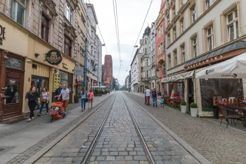 Spacer po starówce Wrocław, ulica z torami tramwajowymi i kamienicami. Rodzina z wózkiem spaceruje po bruku.