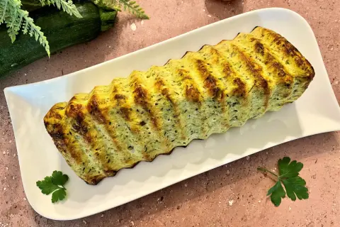 Un délicieux pain de courgettes, doré et savoureux, servi sur une assiette blanche. Parfait pour un repas léger.