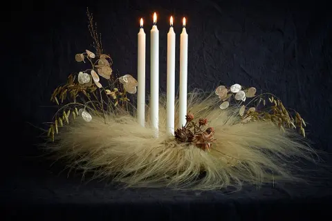 Ausgefallener Adventskranz Trend: Vier weiße Kerzen auf einem Bett aus Federn und Gräsern, geschmückt mit Lunaria und Zapfen.