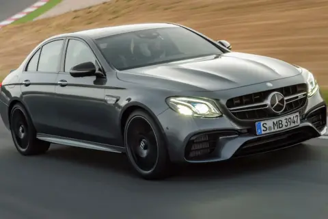 Szary Mercedes-Benz E63 AMG na torze wyścigowym, z kierowcą w kasku za kierownicą.