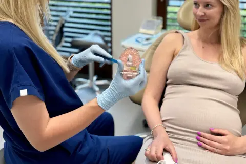 Dentystka pokazuje ciężarnej pacjentce model szczęki, omawiając higienę jamy ustnej. Piaskowanie zębów w ciąży jest bezpieczne i zalecane.