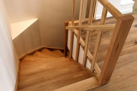 Holztreppe mit geschwungenen Stufen und einem hölzernen Geländer. Die Treppenstufen streichen das Licht und laden zum Hinaufgehen ein.