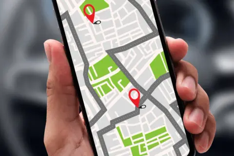 Dłoń trzyma smartfon z mapą i pinezkami. Dowiedz się, jak namierzyć telefon po numerze, by zawsze wiedzieć, gdzie jest bliska osoba.