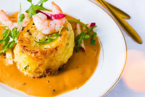 Un délicieux soufflé de crabe, nappé d'une bisque onctueuse et garni de crevettes et de roquette.