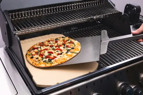 Pyszne ciasto na grilla z kurczakiem, suszonymi pomidorami i oliwkami jest wsuwane na kamień do pizzy.