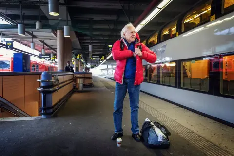 Äldre man i röd jacka på tågstationen, kanske på väg att resa som Kay Pollack.