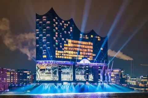 Elbphilharmonie, konserthus Hamburg, badar i ljus och strålkastare över vattnet en mörk kväll.