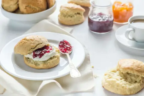 Ein Scone mit Clotted Cream und Marmelade, daneben eine Tasse Kaffee und weitere Scones.