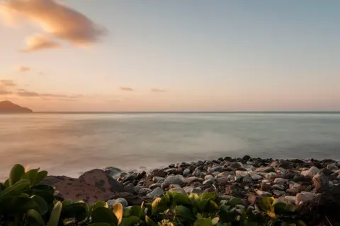 Coucher de soleil sur une plage de galets, avec des îles au loin. Les **filtres photo** accentuent les tons pastel du ciel et la douceur de l'eau.