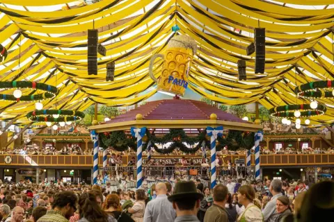 Festa della birra a Monaco: un'enorme folla festeggia sotto un tendone decorato con festoni gialli e neri, dominato da un gigantesco boccale di birra.