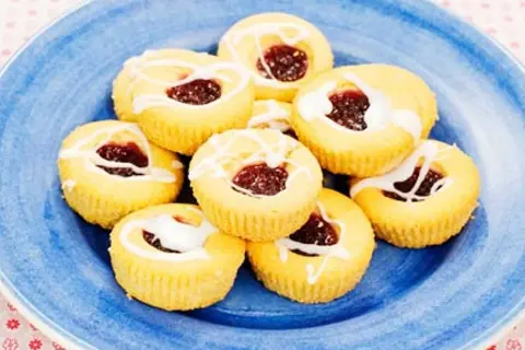Hallongrottor recept: små, runda kakor med hallonsylt i mitten och glasyr på en blå tallrik.