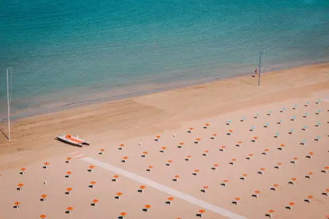 Pusta plaża w Rimini z rzędem pomarańczowych parasoli i łodzią motorową.