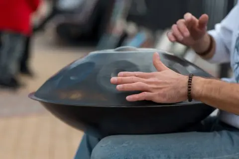 Mann spielt auf einem Hang, einem der ausgefallenen Blasinstrumente, das wie eine UFO-förmige Trommel aussieht.