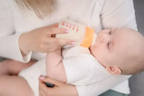 Mama karmi dziecko butelką z mlekiem. Na butelce widać miarkę, jak przy wycofanym mleku Bebilon.