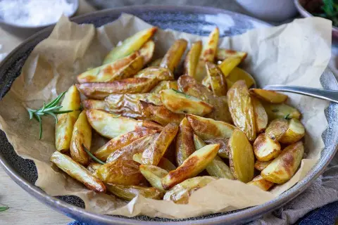 Krispiga klyftpotatis i airfryer, gyllene och redo att serveras med en kvist rosmarin.
