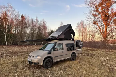 Zmodyfikowany caddy kamper z namiotem dachowym i panelem słonecznym gotowy na przygodę w lesie.