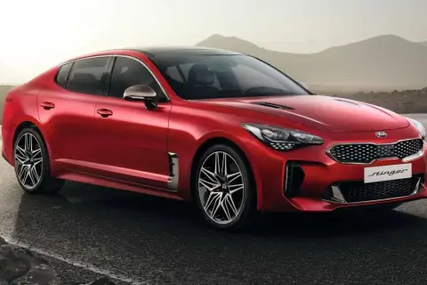 Kia Stinger CV rojo brillante, con llantas deportivas, aparcado en una carretera mojada con montañas al fondo.