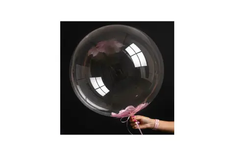 Przezroczysty bubble balon z różowymi płatkami kwiatów w środku i na dole, trzymany przez dłoń.