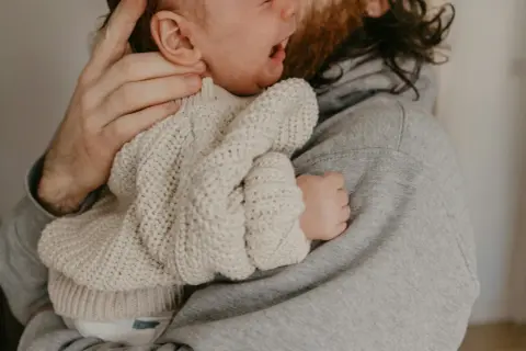 En pappa tröstar sitt ledsna barn som verkar ha bebis hård i magen.