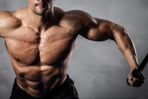Uomo muscoloso con addominali scolpiti, che si allena con cavi. Ideale per chi cerca recupero e crescita muscolare con aminoacidi dopo allenamento.
