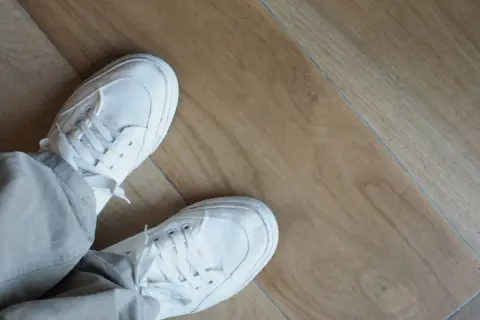 Piedi con scarpe bianche su un pavimento in laminato effetto legno. Questo pavimento spc cos'è? È un materiale resistente e moderno.