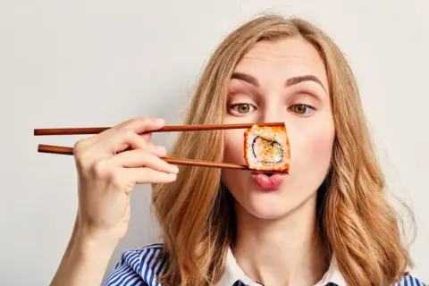 Kobieta z pałeczkami trzyma sushi przed ustami, zastanawiając się, czy sushi jest kaloryczne.