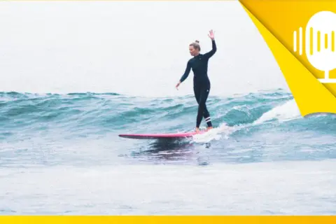 Surferin auf einer rosa Tafel, die mit erhobener Hand über die Wellen gleitet. Ein Symbol für das Lebensfreude wiederfinden.
