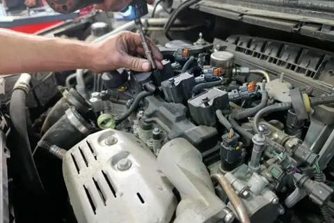 Mécanicien utilisant une visseuse pour changer les bougies d'allumage essence. Un moteur de voiture est visible.