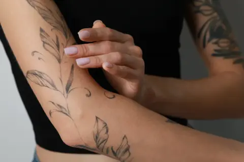 Ein frisches Tattoo mit Blattmotiven ziert den Arm einer Person, die schwarze Kleidung trägt.
