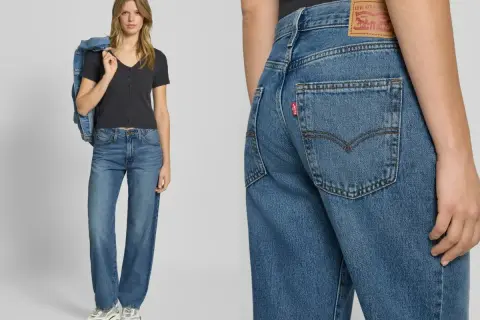Modelka w jeansach Levi's i czarnej bluzce, z kurtką dżinsową na ramieniu. Detal zbliżenia na tył spodni z charakterystyczną czerwoną metką.