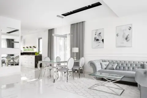 Eleganckie, nowoczesne wnętrze w stylu glamour. Błyszczące płytki, szara sofa i szklany stół tworzą luksusową atmosferę.