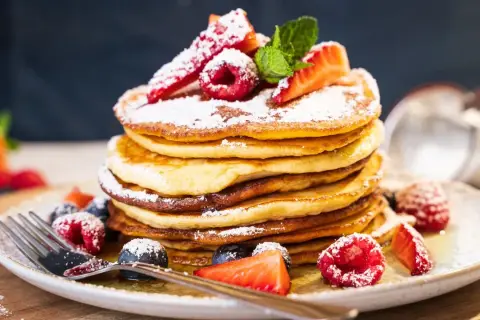 Ein Stapel amerikanischer Pancakes, bestäubt mit Puderzucker und garniert mit frischen Beeren und Minze.