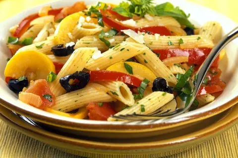 Bunte Nudelgerichte mit Penne, Tomaten, Zucchini, schwarzen Oliven und frischen Kräutern, garniert mit Parmesan.