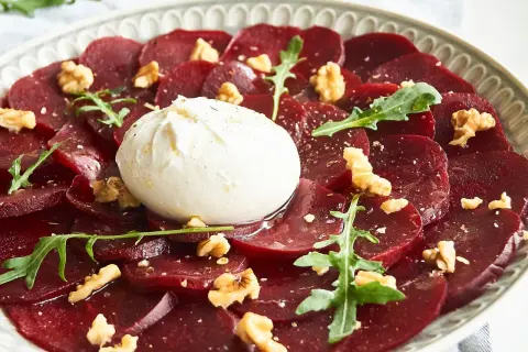 Rote Bete Carpaccio mit Burrata, Walnüssen und Rucola auf einem Teller.