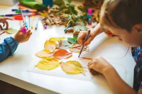 Niños creando arte con hojas de otoño. Actividades para trabajar las plantas en infantil, usando rotuladores y hojas secas para dibujar.