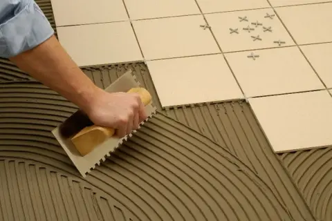 Mano extendiendo cemento cola con llana para poner azulejos.