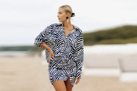 Kobieta o figurze klepsydry plus size w sukience w panterkę na plaży.