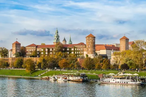 Wawel zwiedzanie z przewodnikiem. Widok na zamek i Wisłę z łodziami w jesiennej scenerii.