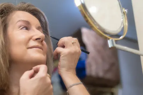 Kobieta po 50. roku życia poprawia makijaż, delikatnie podkreślając oczy. Widać subtelne zmiany skórne na twarzy, które dodają jej charakteru.