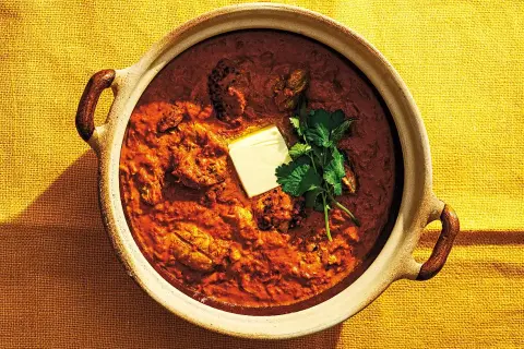 En skål med krämig chicken tikka masala, toppad med en smörbit och färsk koriander. Perfekt för en mysig middag.