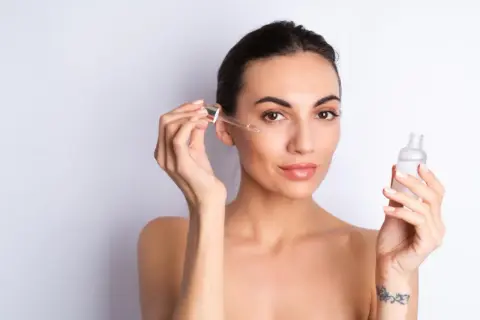 Kobieta aplikuje na twarz serum z peptydami. Skóra wygląda na nawilżoną i promienną.