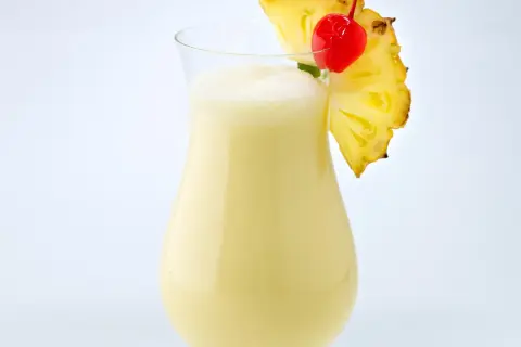 Cremiger Pina Colada mit Ananasstück und Kirsche garniert.