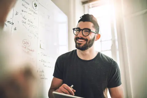 Ein Mann mit Brille lächelt vor einer Tafel mit Notizen zur Fernuni Wirtschaftsinformatik.