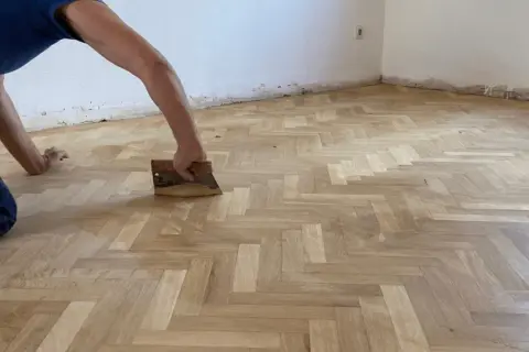Trabajador aplicando barniz a un suelo de parquet en espiga. Consulta el precio lijado y barnizado parquet para renovar tu hogar.