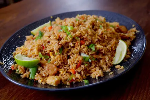 En tallrik med khao pad, en smakrik thailändsk stekt risrätt med kyckling, grönsaker och limeklyftor.