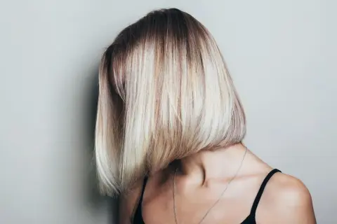 Kobieta z asymetryczną, blond fryzurą typu bob, z ciemniejszymi odrostami.